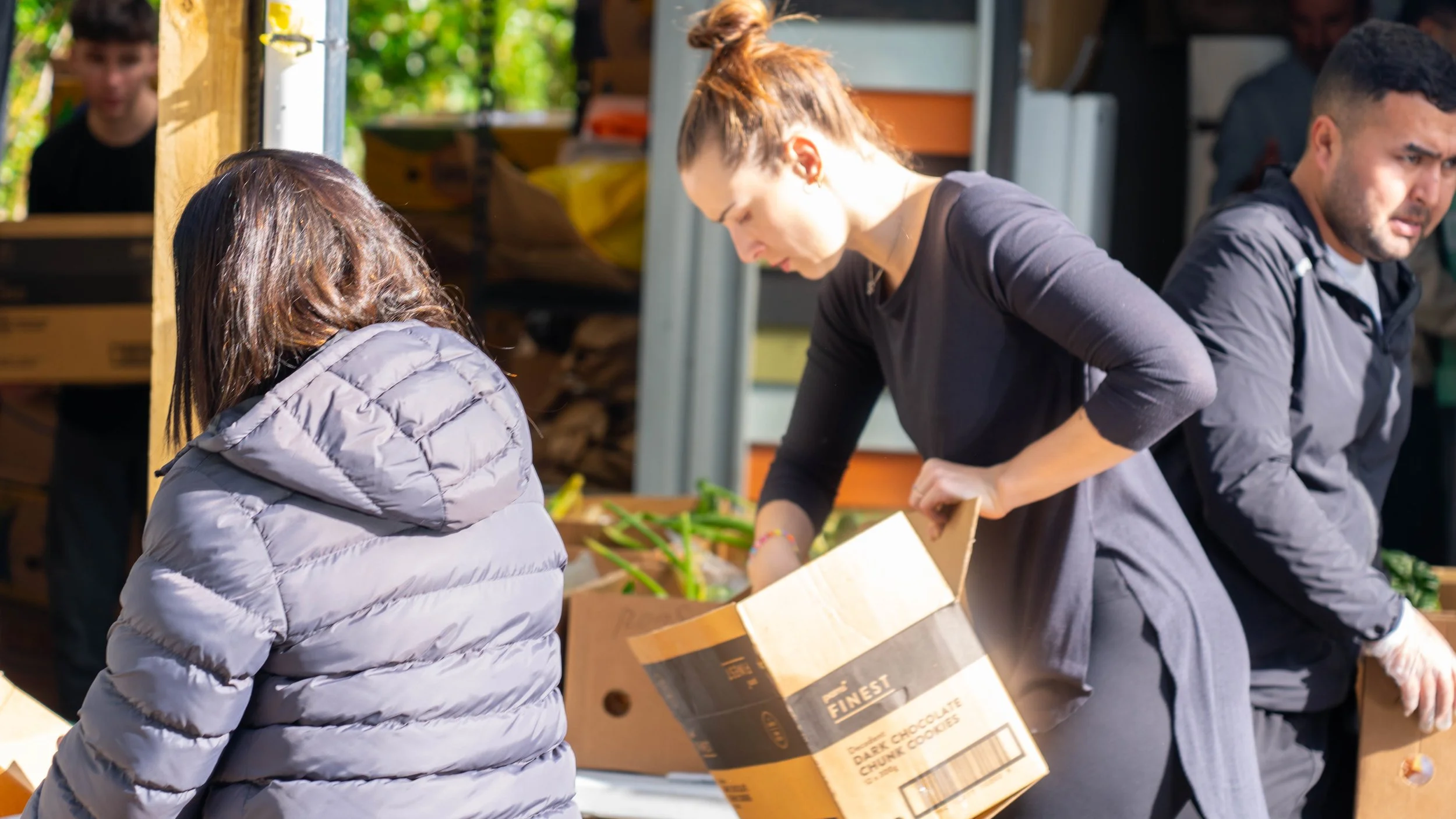 two women and a man unload a box of fresh, donated fruit and vegetables provided by KiwiHarvest 