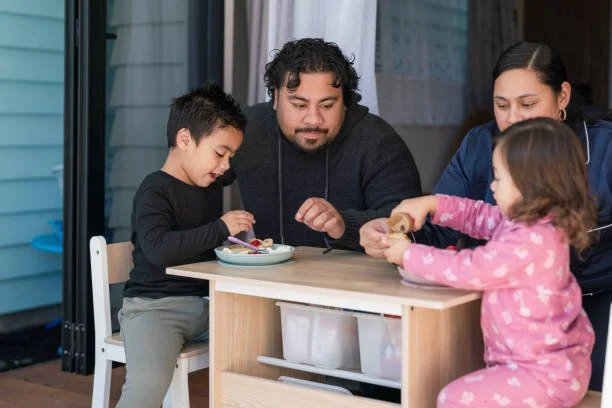 A family sits down together and eats a meal with their two young children