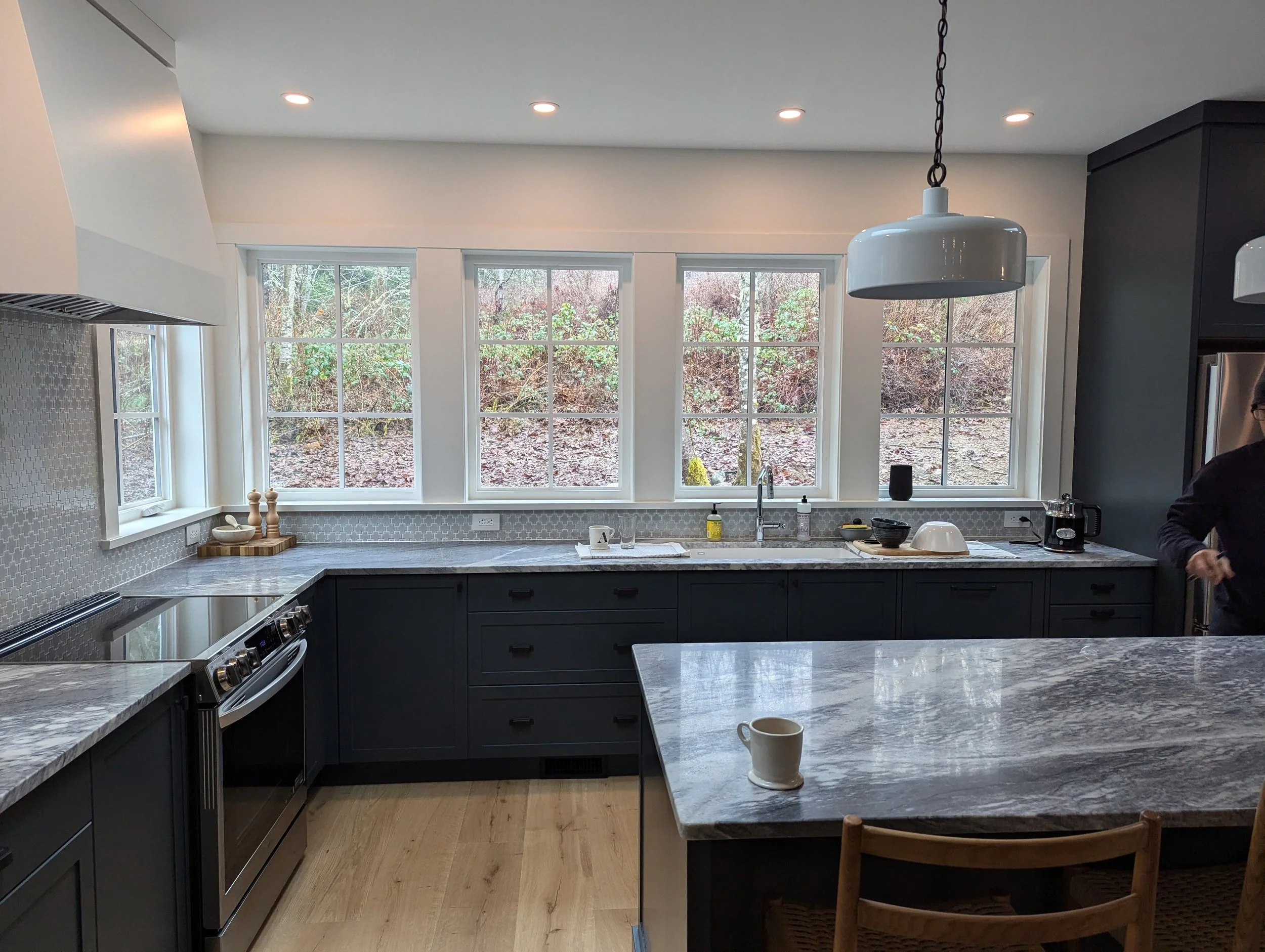 Modern black-and-gray kitchen with marble countertops, large windows, pendant lighting, island seating, and stainless steel appliances
