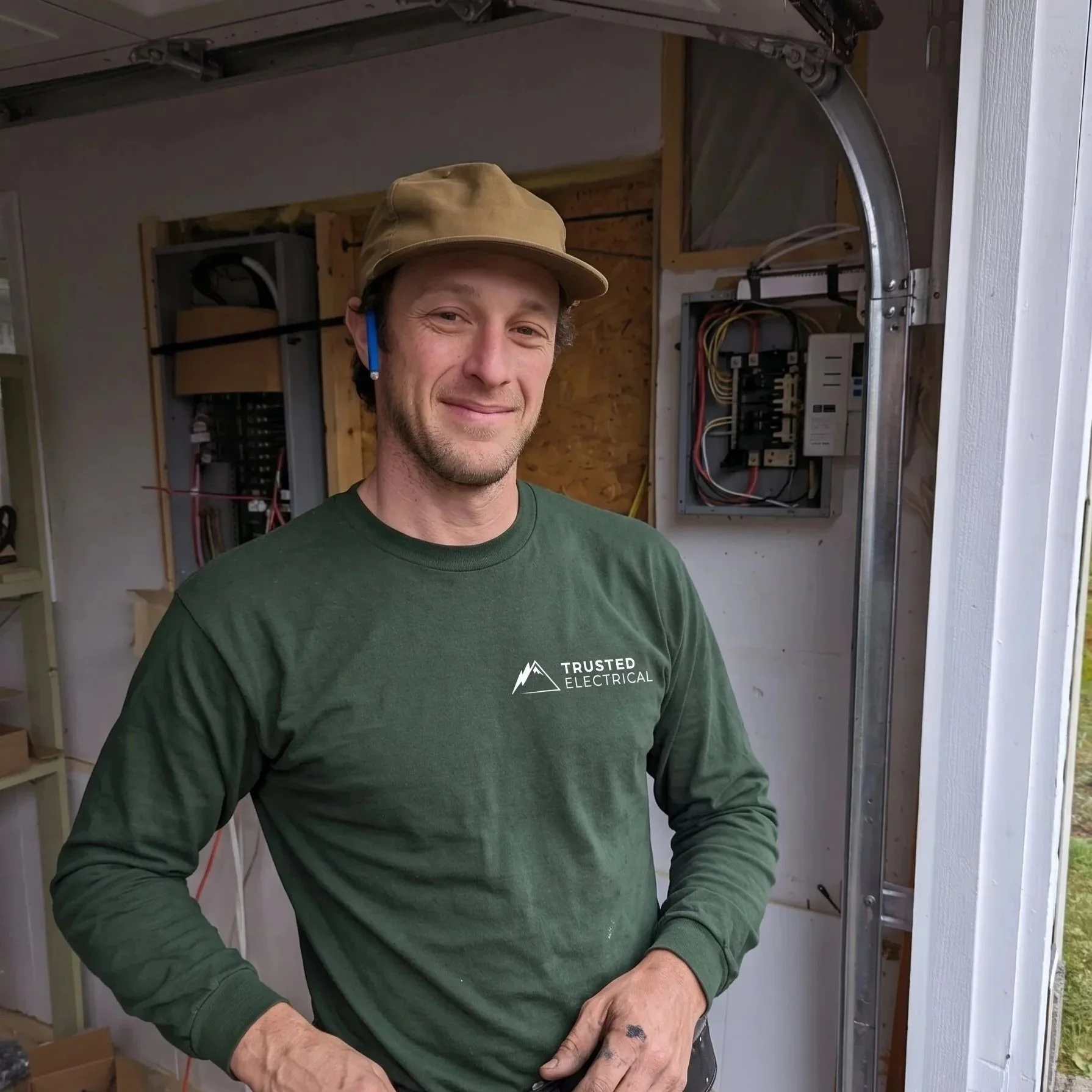 Courtenay Electrician wearing a Trusted Electrical shirt and safety glasses stands inside a trailer with exposed electrical panels.