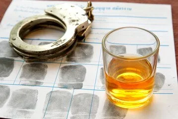 Handcuffs and a glass of whiskey on a fingerprint chart