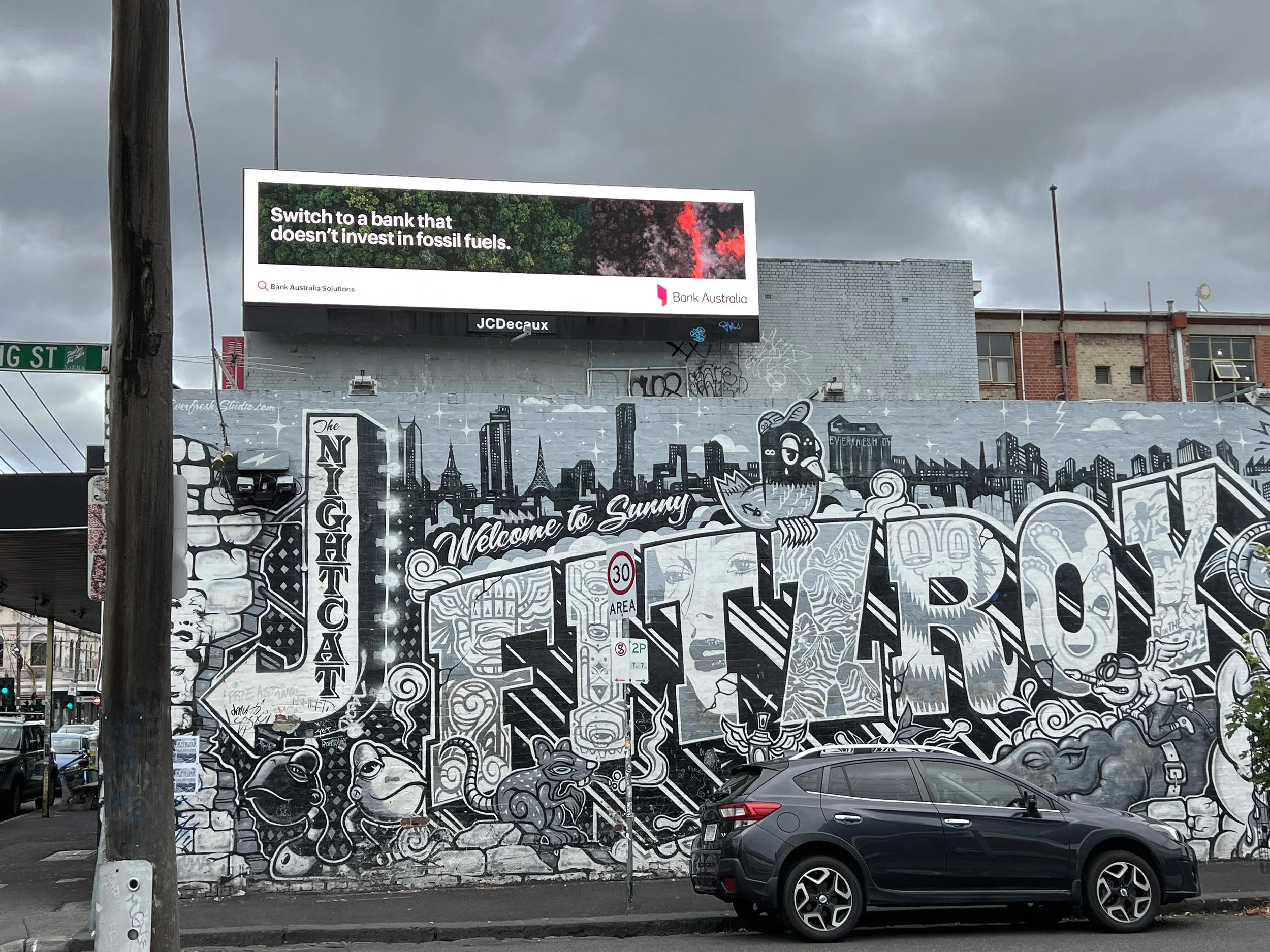 Black and white mural of New York City skyline with cartoon characters and graffiti, and a car parked in front.