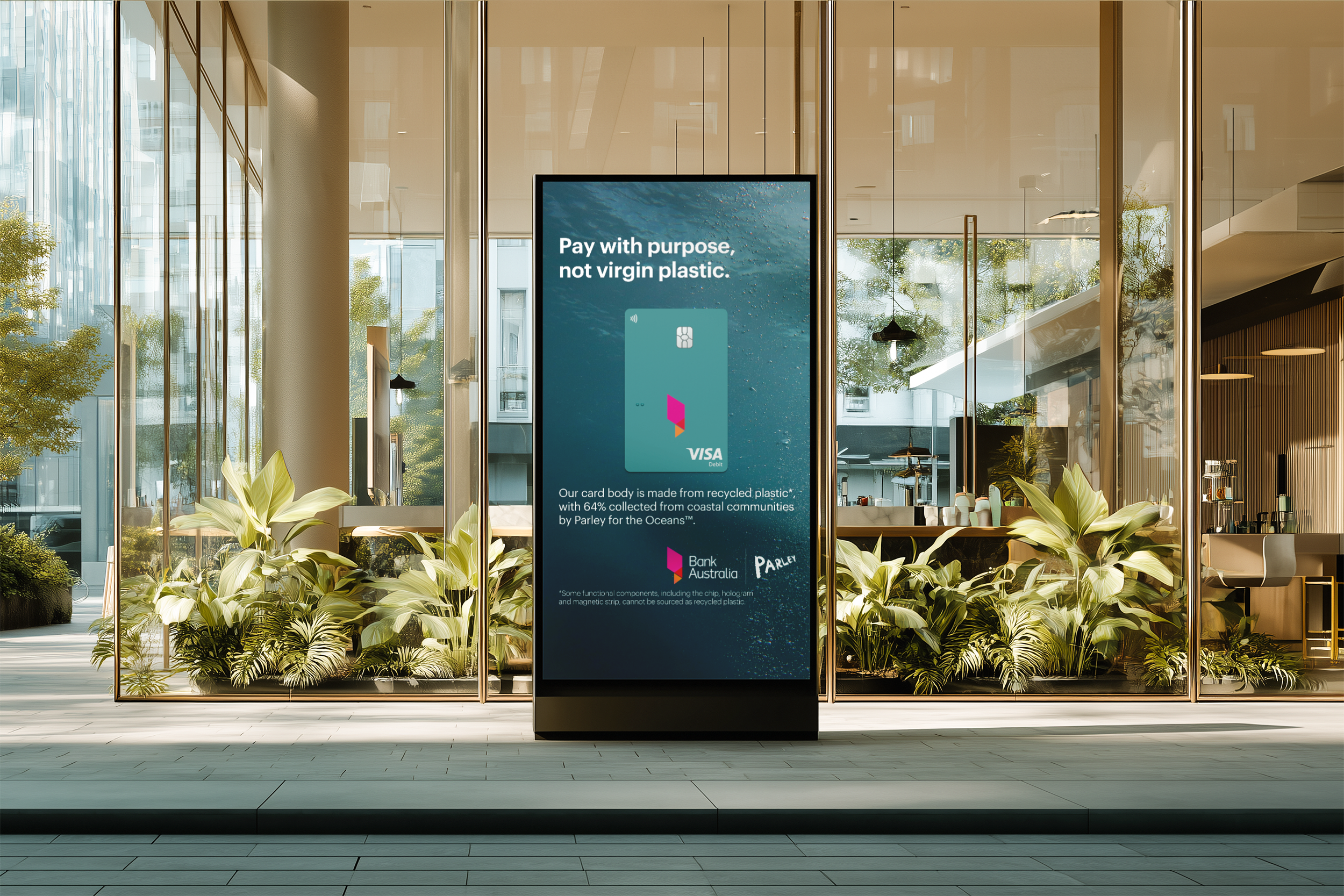 Digital advertisement display in a modern glass-walled building lobby promoting environmentally-friendly payment cards made from recycled plastic, with logos of VISA and Bank Australia.
