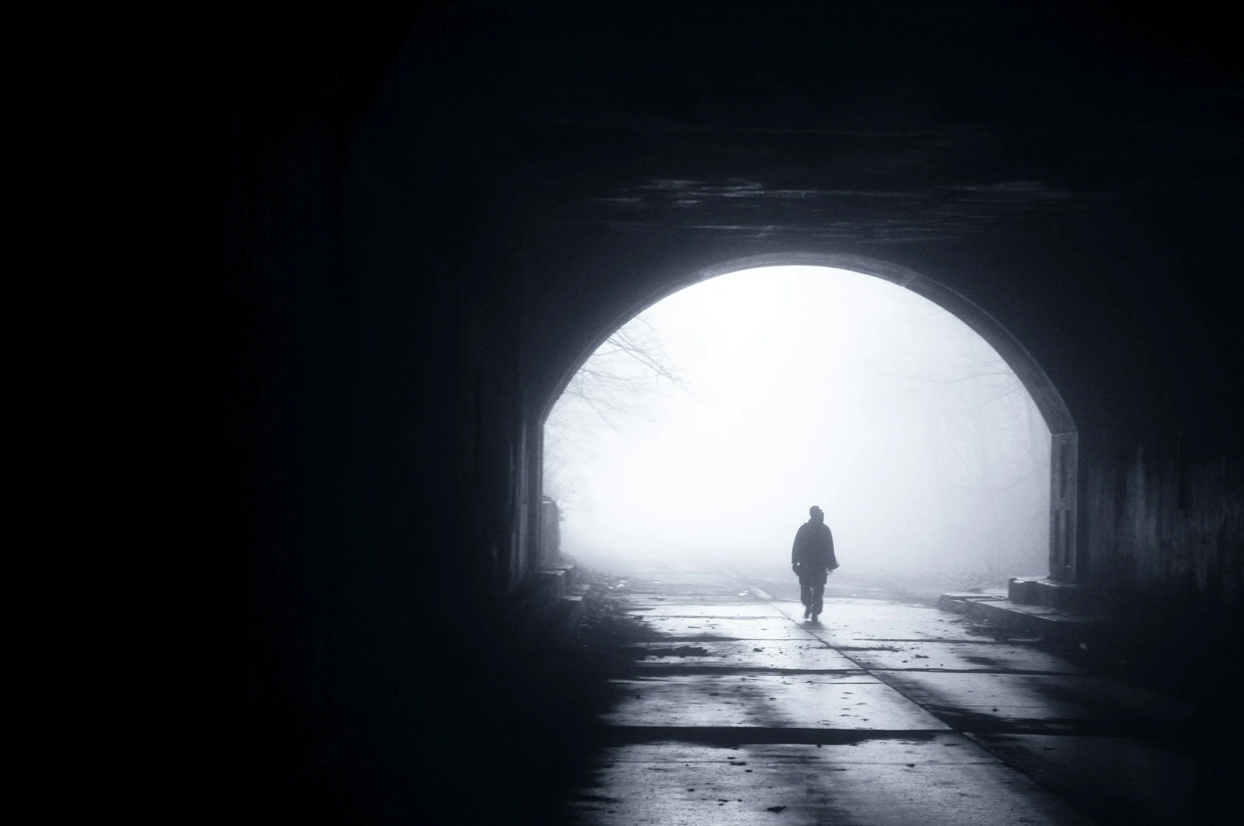 A person walking through a dark tunnel toward bright light at the exit, with mist or fog outside.