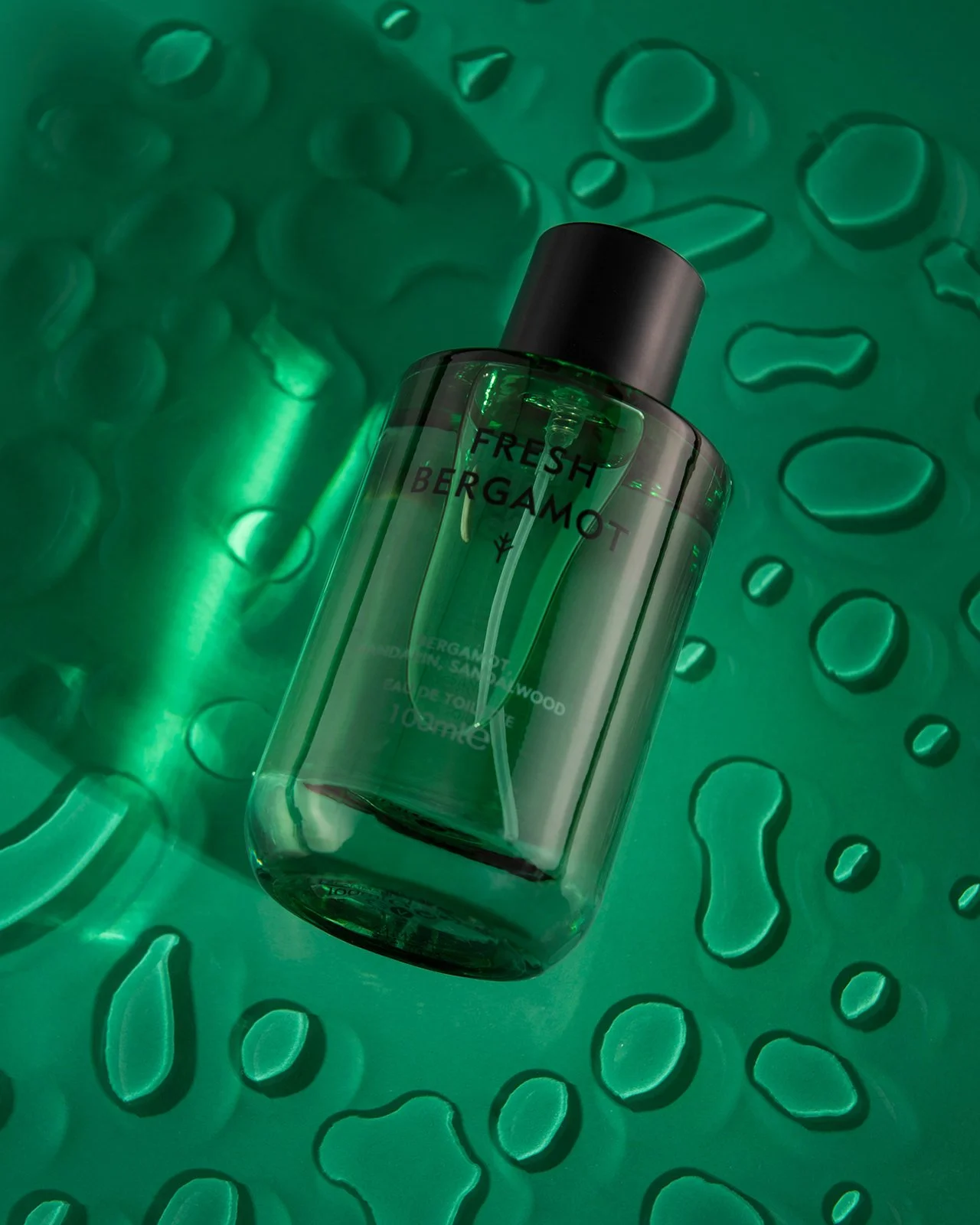 hero product photography cosmetics for fresh bergamot aftershave on a green background with drops of water on the surface