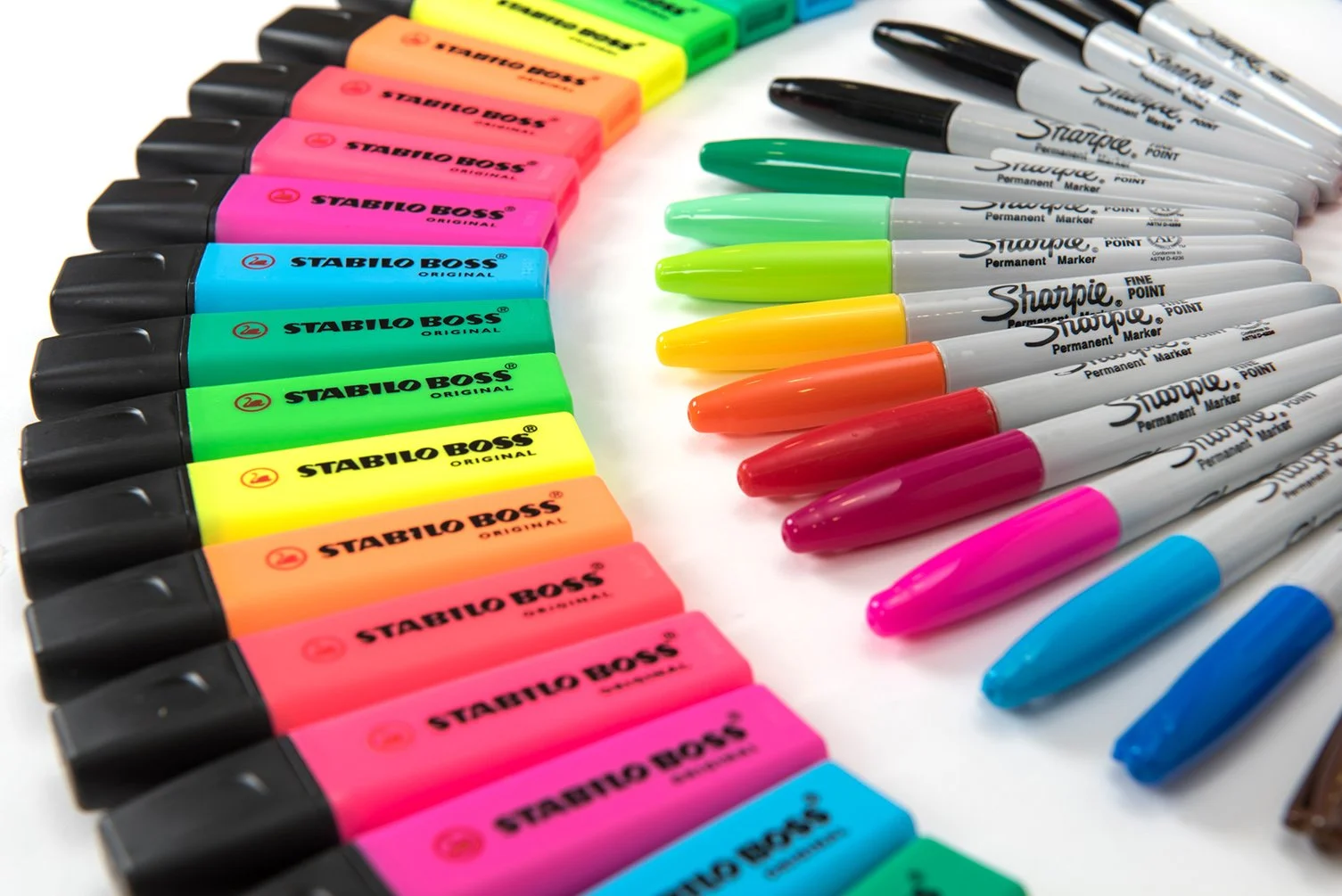 product photography shot showing a colourful spread of pens stationary sharpie and highlighters arranged in a circular rainbow on a white background