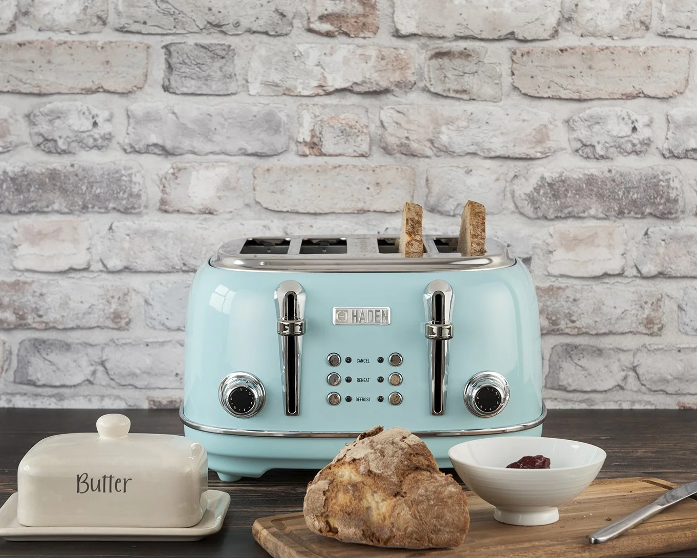 lifestyle photography shot showing a light blue kettle and toaster in a kitchen setting with props on a dark wooden surface and light brick background