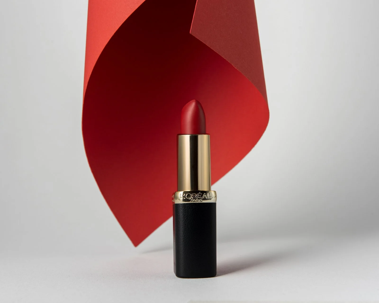 product hero shot showing loreal red lipstick in front of a red folded paper background, on a white surface