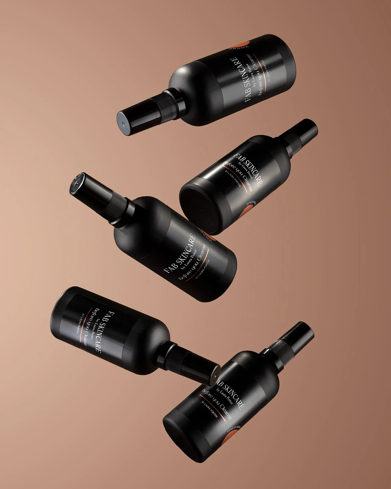 hero product photography four black fab skincare bottles with spray nozzles, arranged diagonally on a graduated brown background