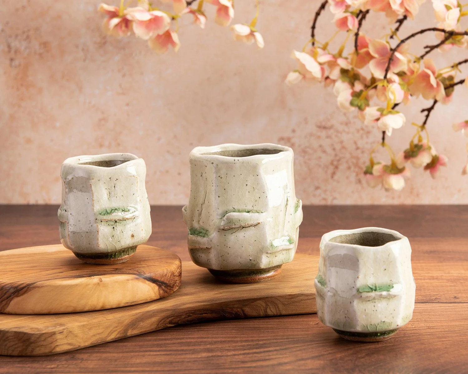 artistic hero photography showing 3 Japanese style drinking cups by ben dodd on a wooden surface and textured backdrop with pink cherry blossom 