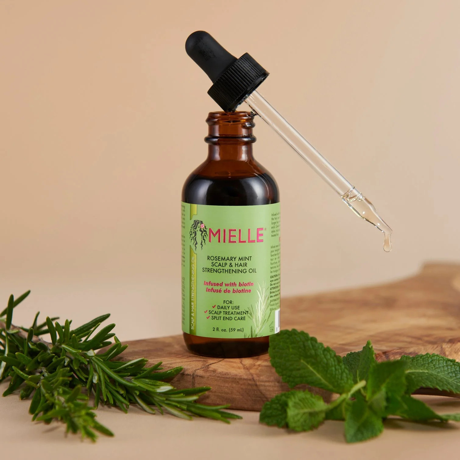 hero product photography showing a bottle of mielle haircare oil with herbs and comb on a wooden plinth with light brown background