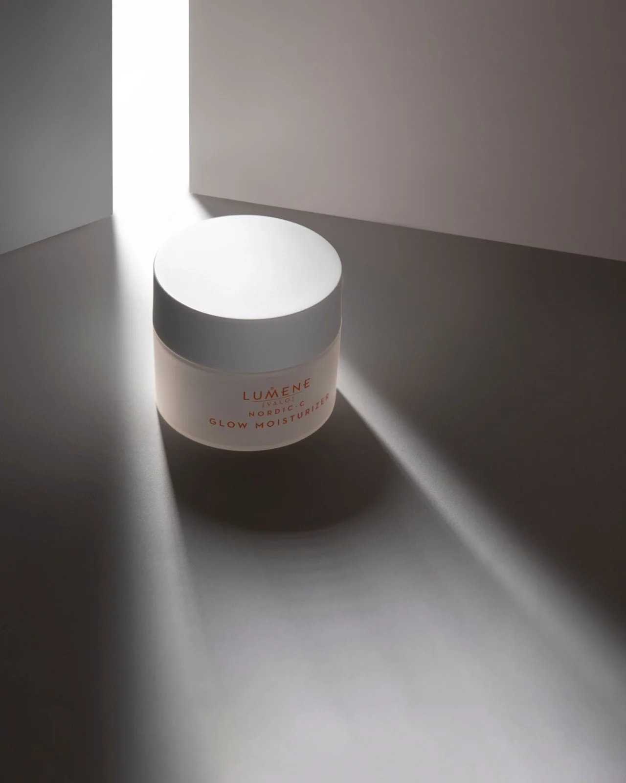 minimal hero product photography with a white tub of lumene nordic glow moisturiser cosmetics with a beam of light illuminating the item