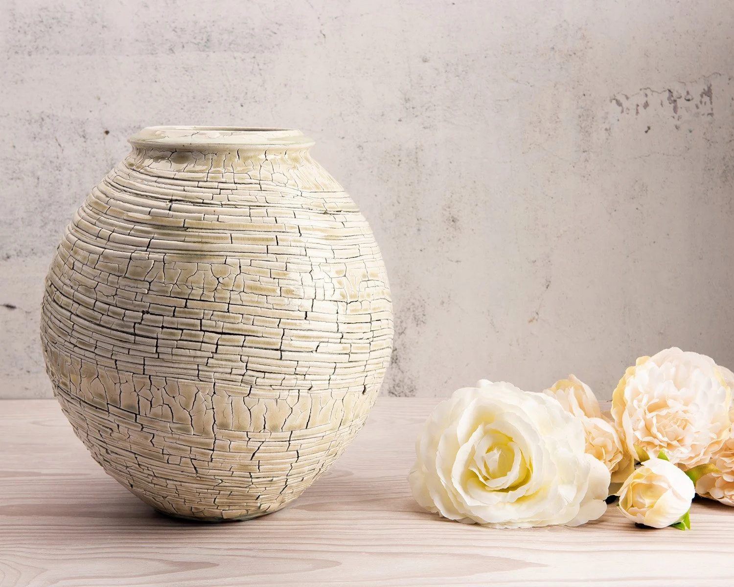 artistic hero photography showing a textured ceramic pot by ben dodd on a light wooden surface and textured background with white roses to the right