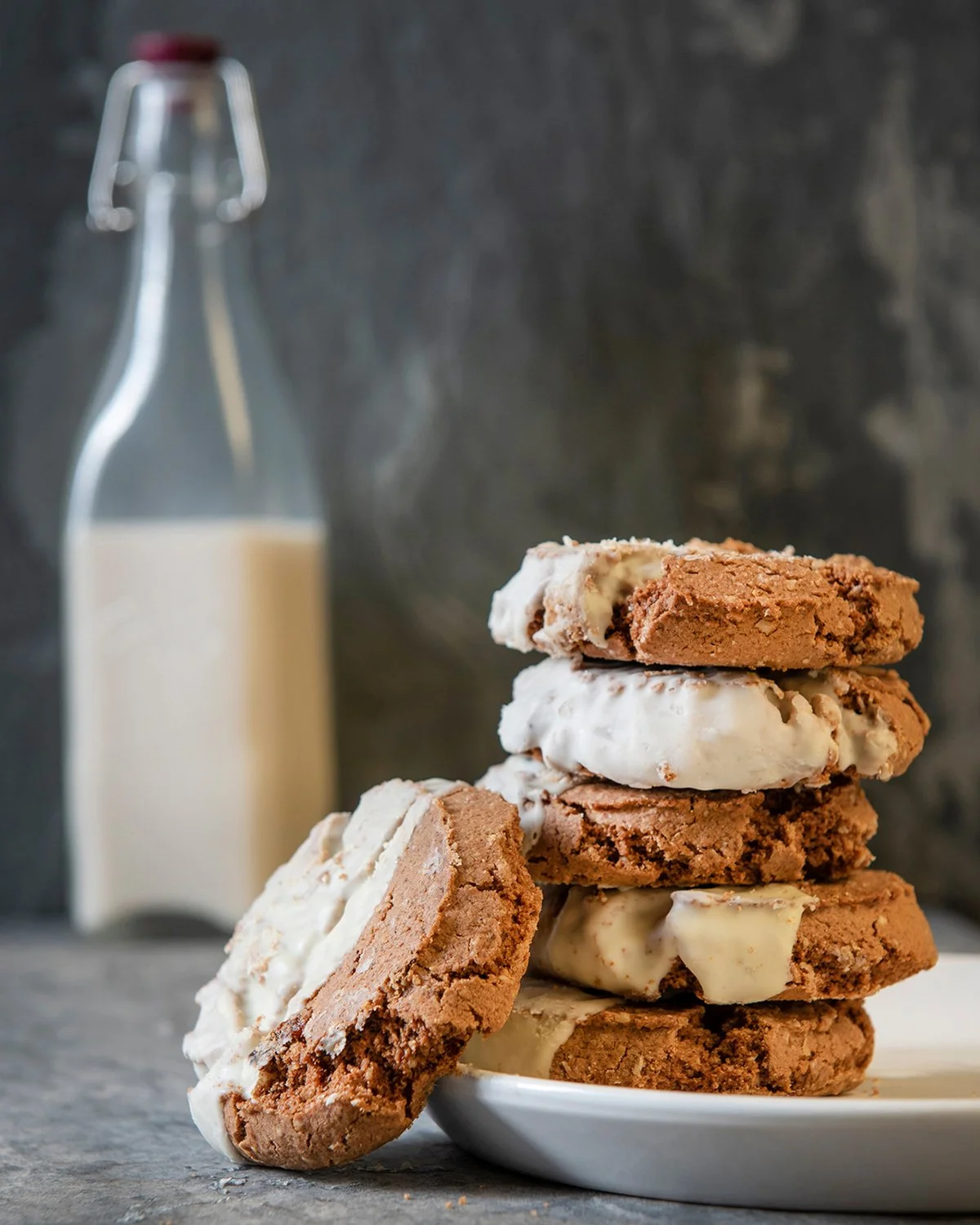 hero food photography showing chunky cookies with white chocolate on a plate with a glass bottle of milk in the background