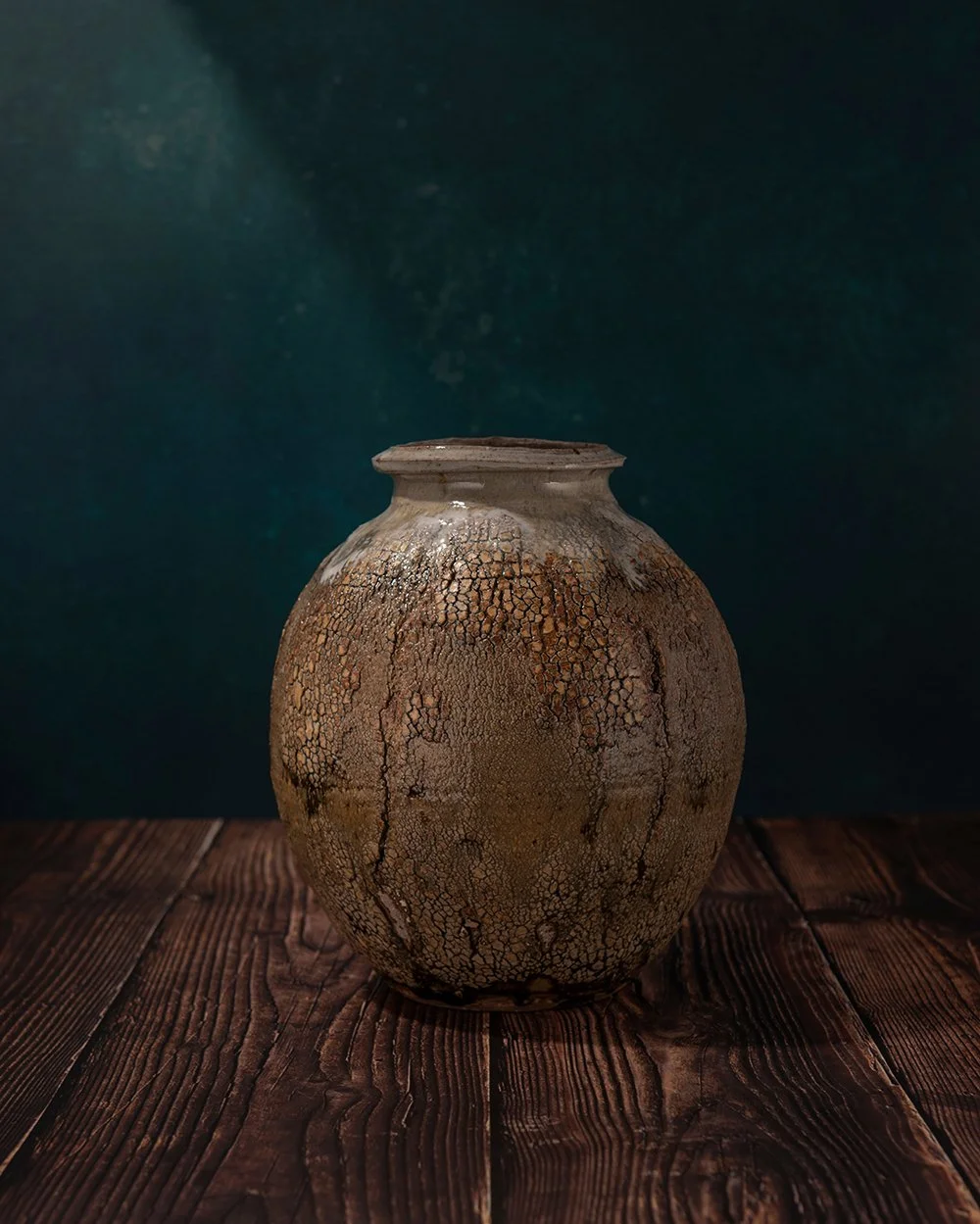artistic product photography showing a textured ceramic pot by ben dodd on a wooden surface and dark green background