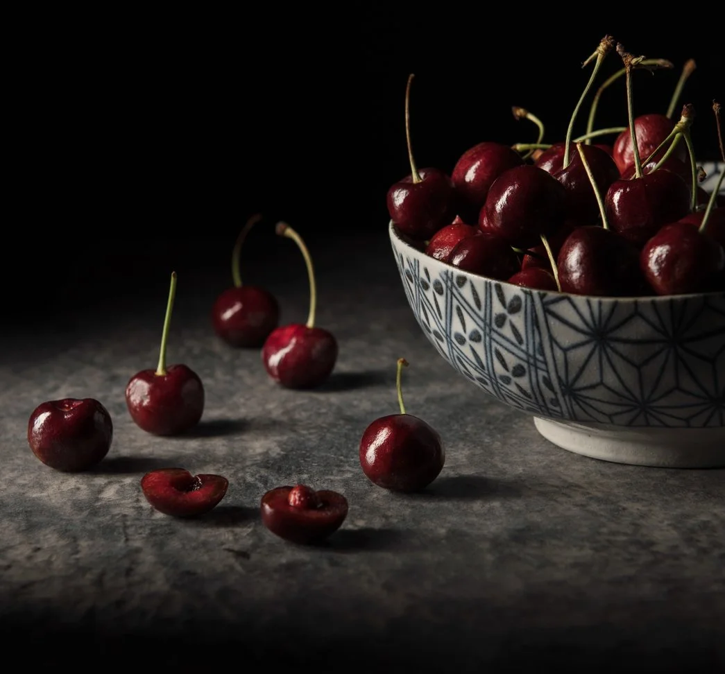hero product photography showing a moroccan designed ceramic bowl full of cherries and dark background with a light source from the left