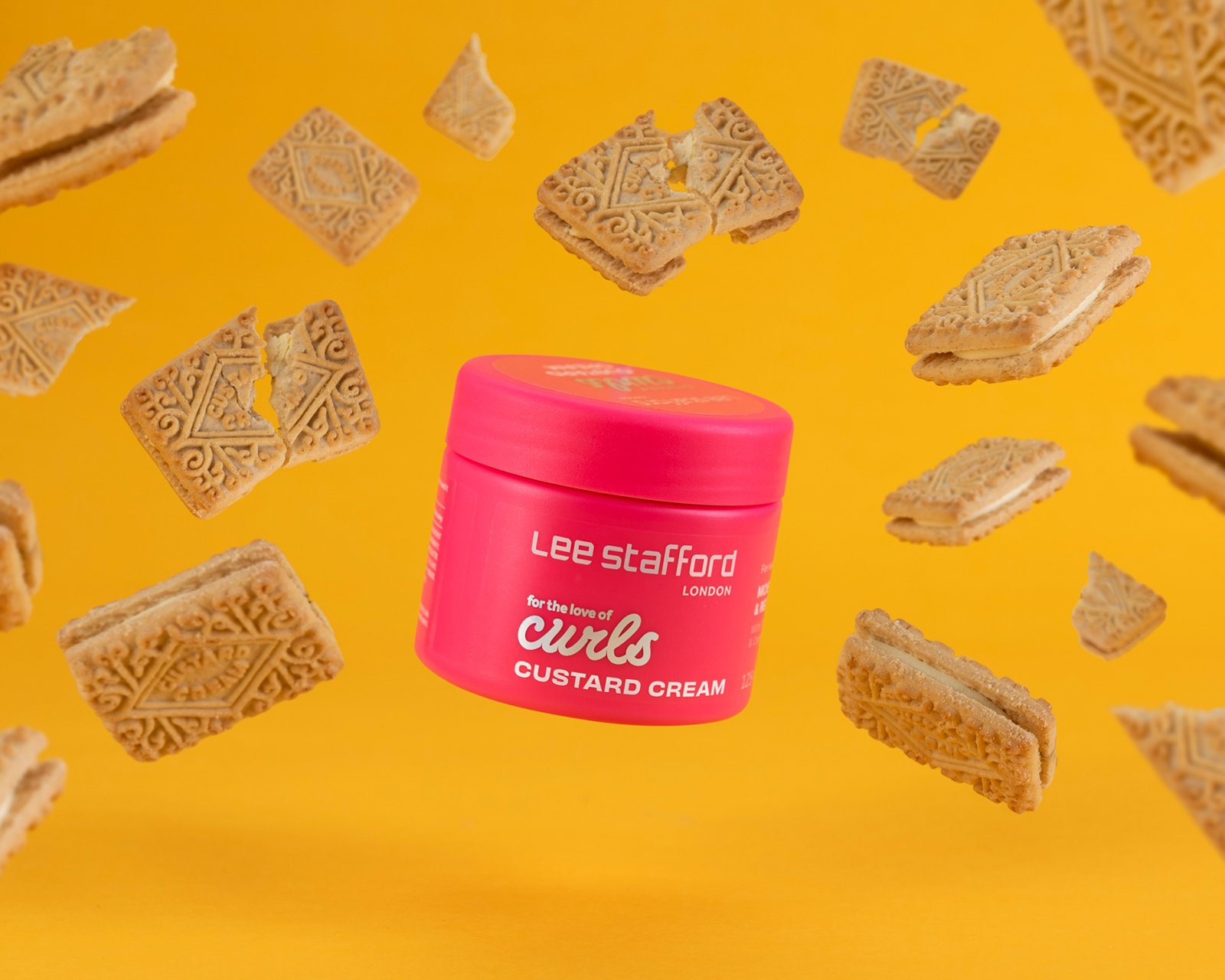 hero product photography showing a pink pot of lee stafford hair curls surrounded by custard cream biscuits on  a graduated yellow background