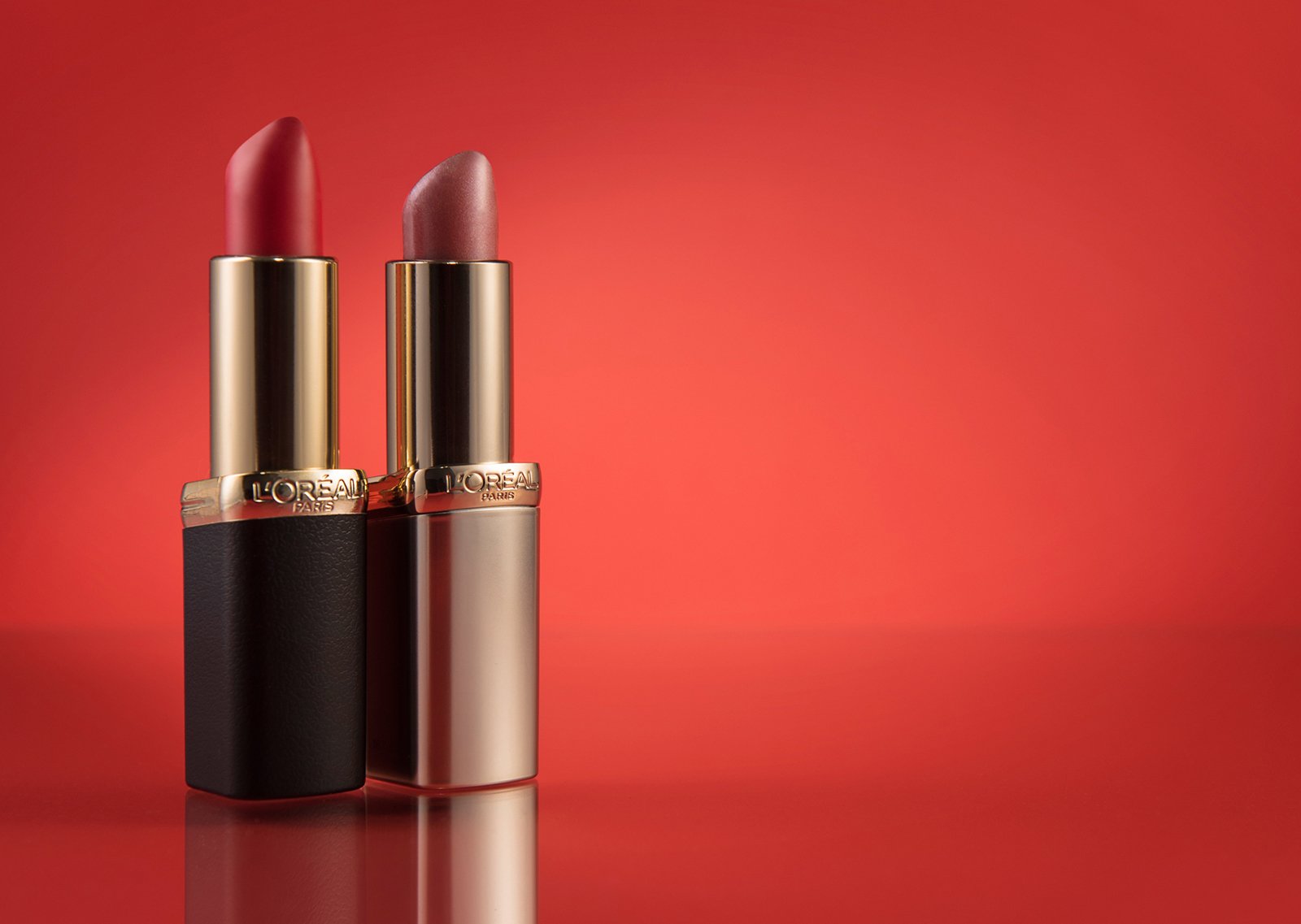 product hero shot showing loreal red and pink lipstick in front of a red graduated background 