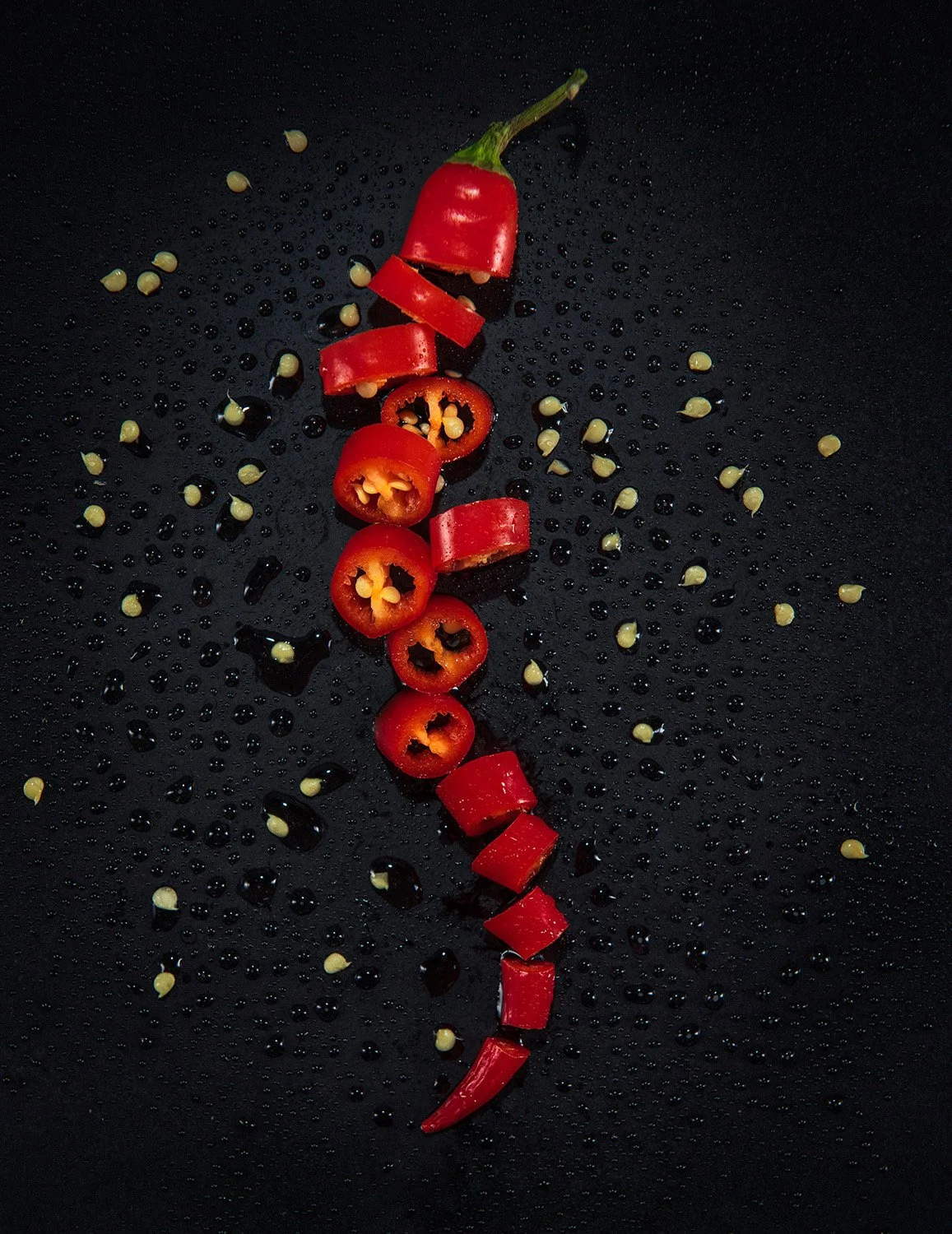 food product photography showing a chopped chilli with seeds spread around on a textured black background