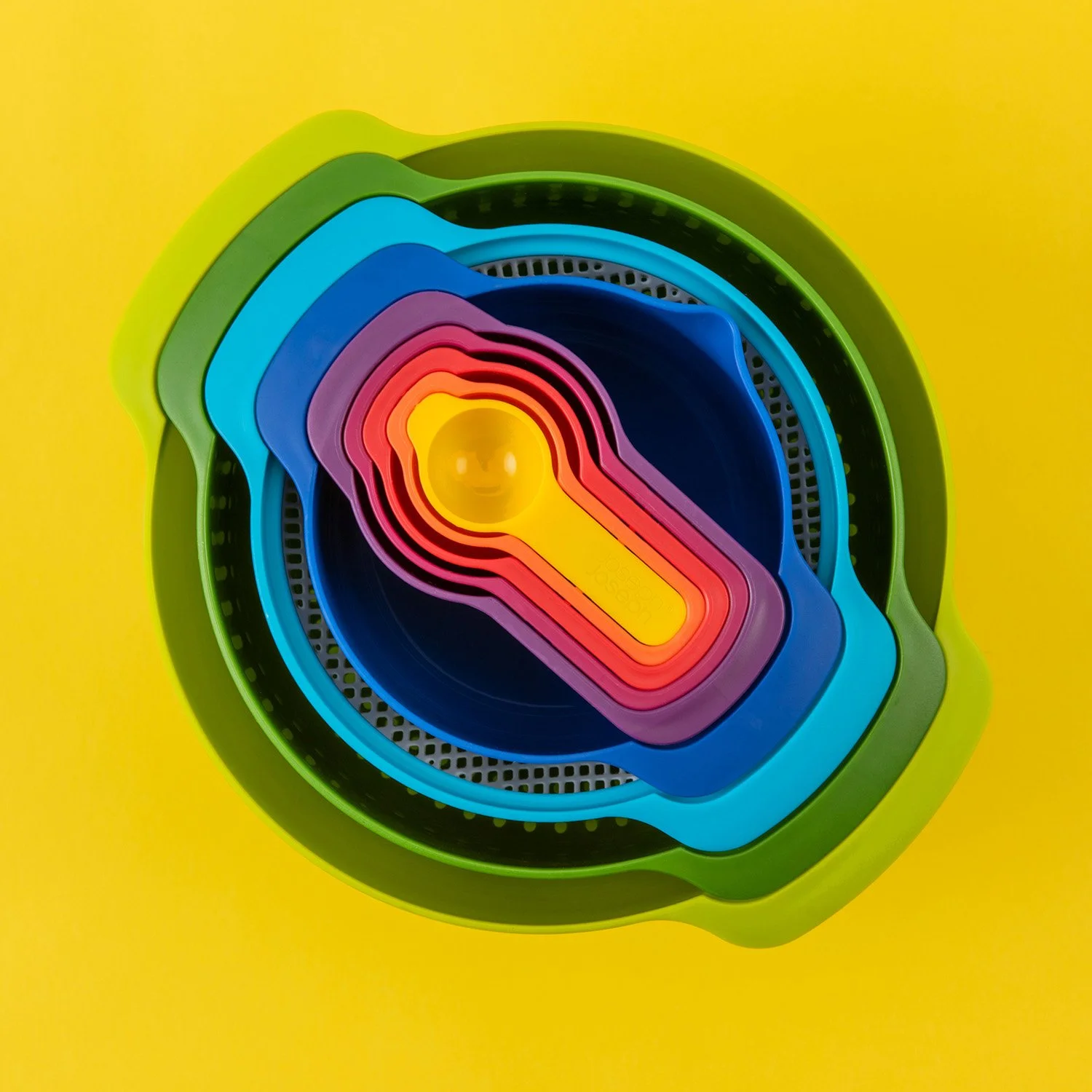 minimal product photography showing a set of stacked colourful plastic kitchenware on a vibrant yellow background