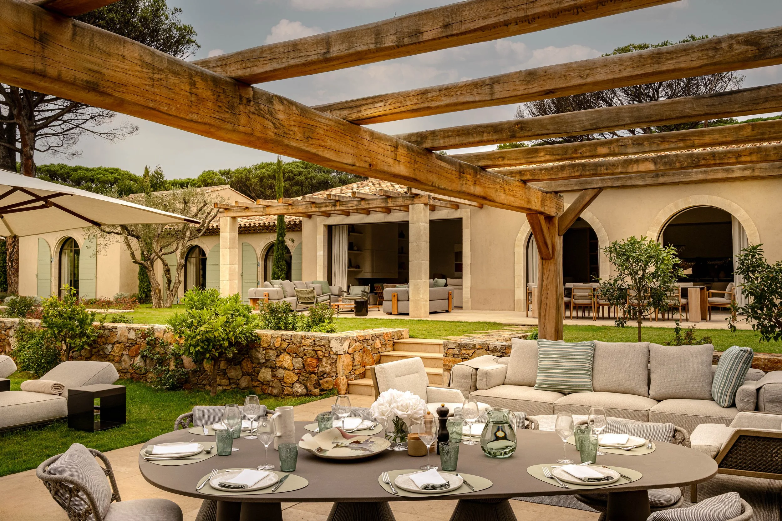 Chambre à coucher élégante avec un grand lit, draps blancs, coussins gris, lampe de chevet en céramique, fenêtre avec rideaux crème, mobilier en bois, tapis beige, décor simple.