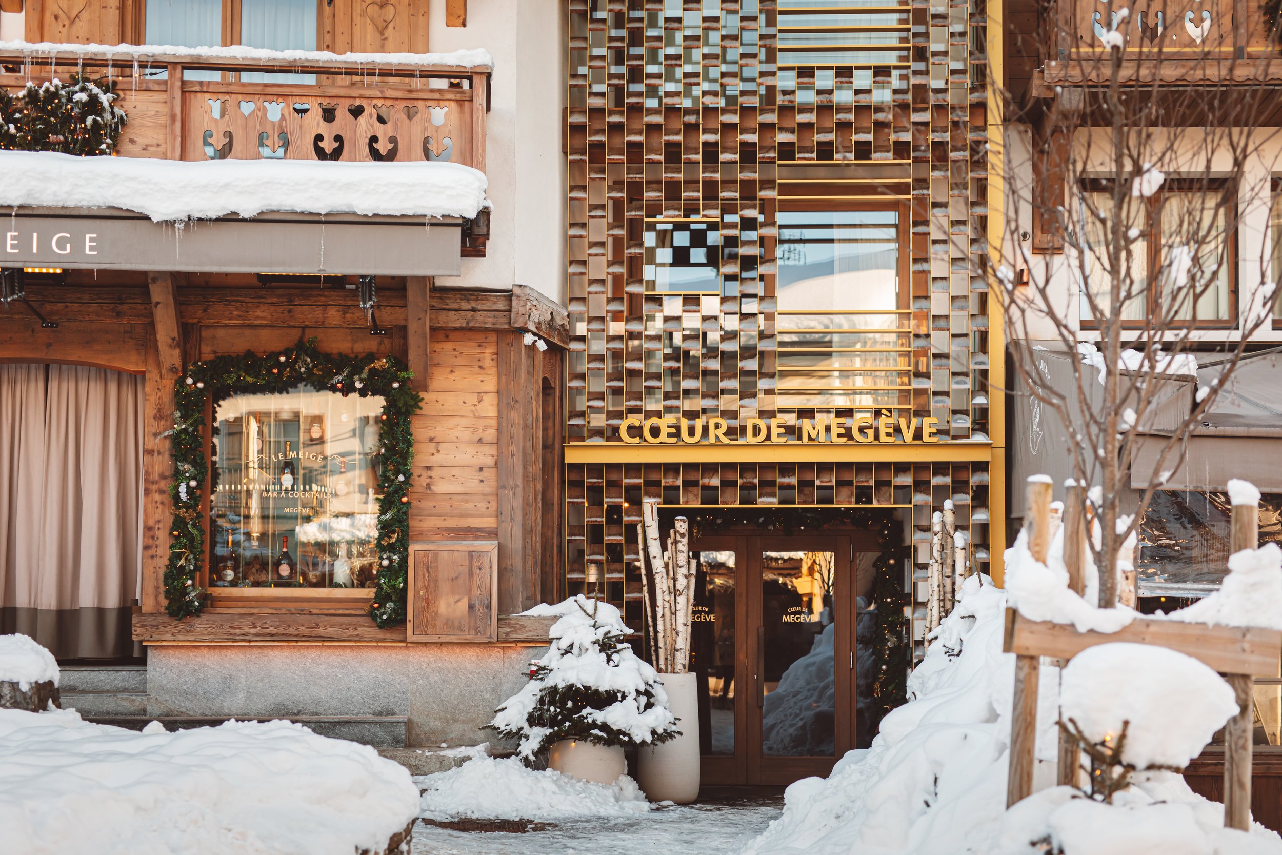 Vue d'un bâtiment en bois avec balcons, neige sur les surfaces, et le texte 'Coeur de Megève' écrit sur la façade.