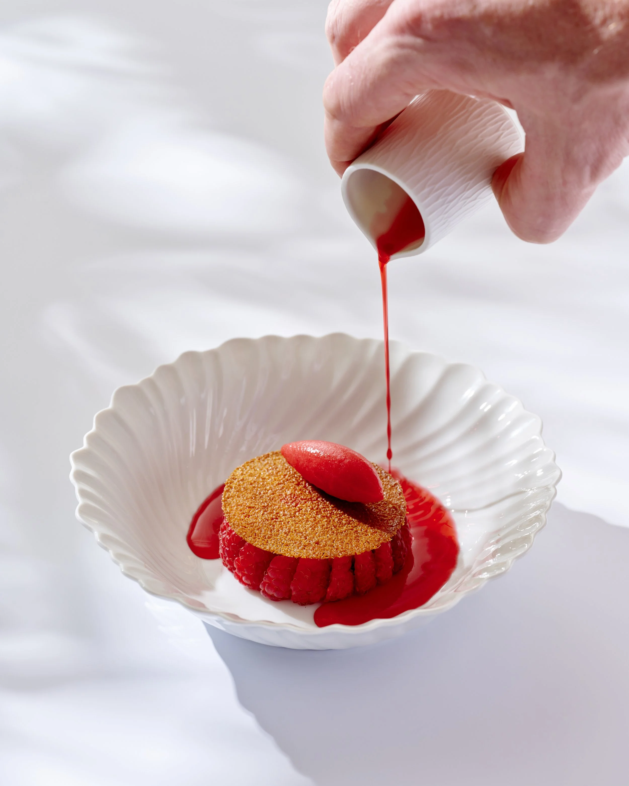 Un chef qui verse un coulis sur un dessert , présentée sur une assiette blanche.