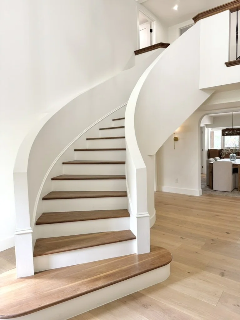 Interior view of a spiral staircase with wooden steps and white walls, leading to the upper floor of a house.