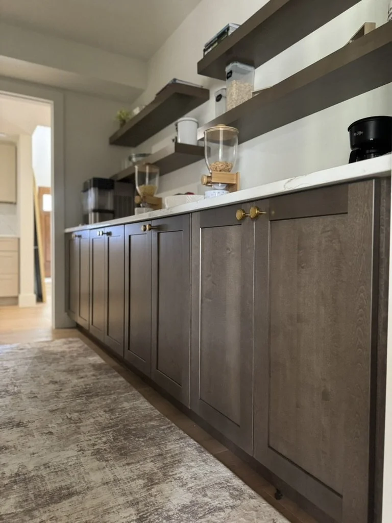 Kitchen countertop with wooden cabinets and floating shelves, containing containers, a coffee grinder, and food storage jars.