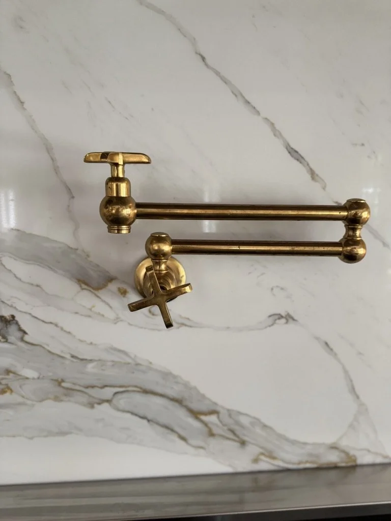 Brass wall-mounted fixture with two horizontal rods and a clamp, mounted on a marble wall.
