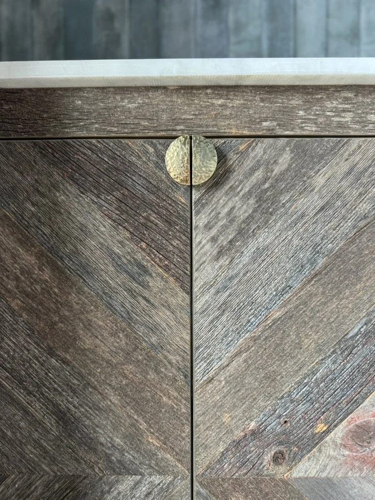 Close-up of a wooden cabinet with a brass circular handle, showing diagonal wood grain patterns.