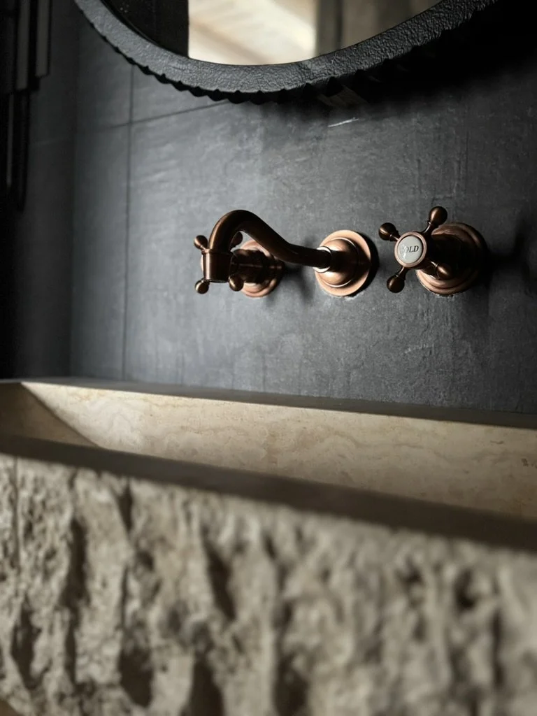 Close-up of a bronze faucet mounted on a dark gray countertop in a bathroom or kitchen.