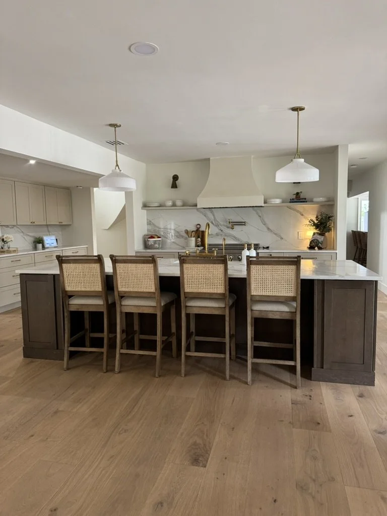 Modern kitchen with a large island, four wooden bar stools with woven backs, white countertops, a marble backsplash, and pendant lights hanging above the island.