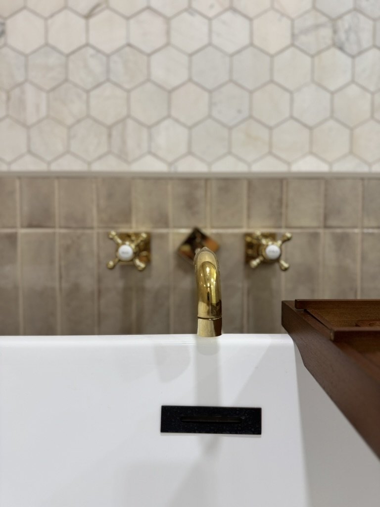 A bathroom sink with a gold faucet and two gold water control handles on a tiled wall.
