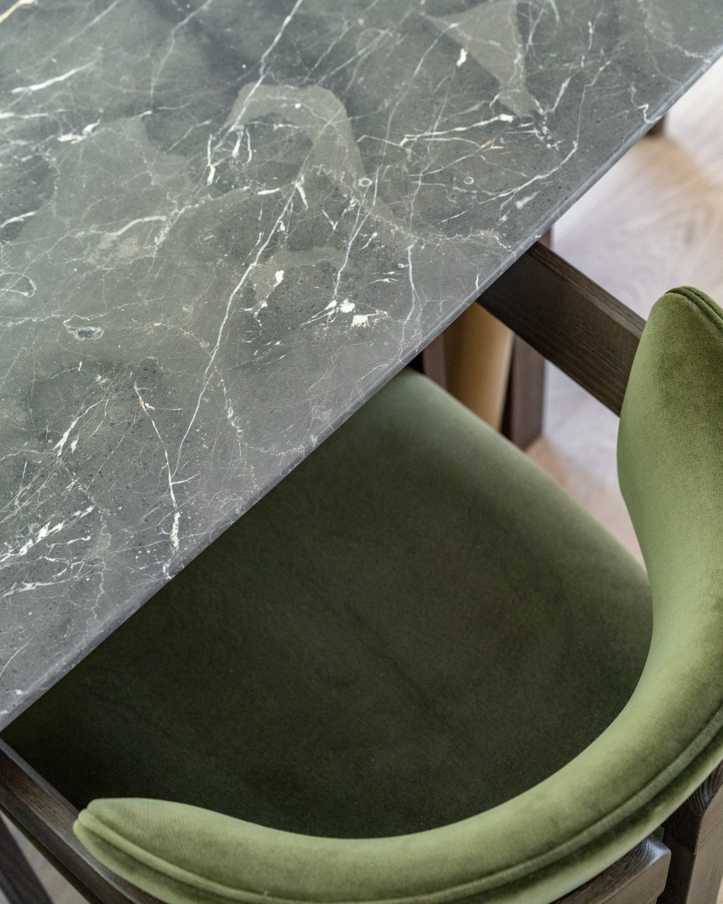 Close-up of a gray marble tabletop with white veining, in front of a green upholstered chair with a curved backrest.