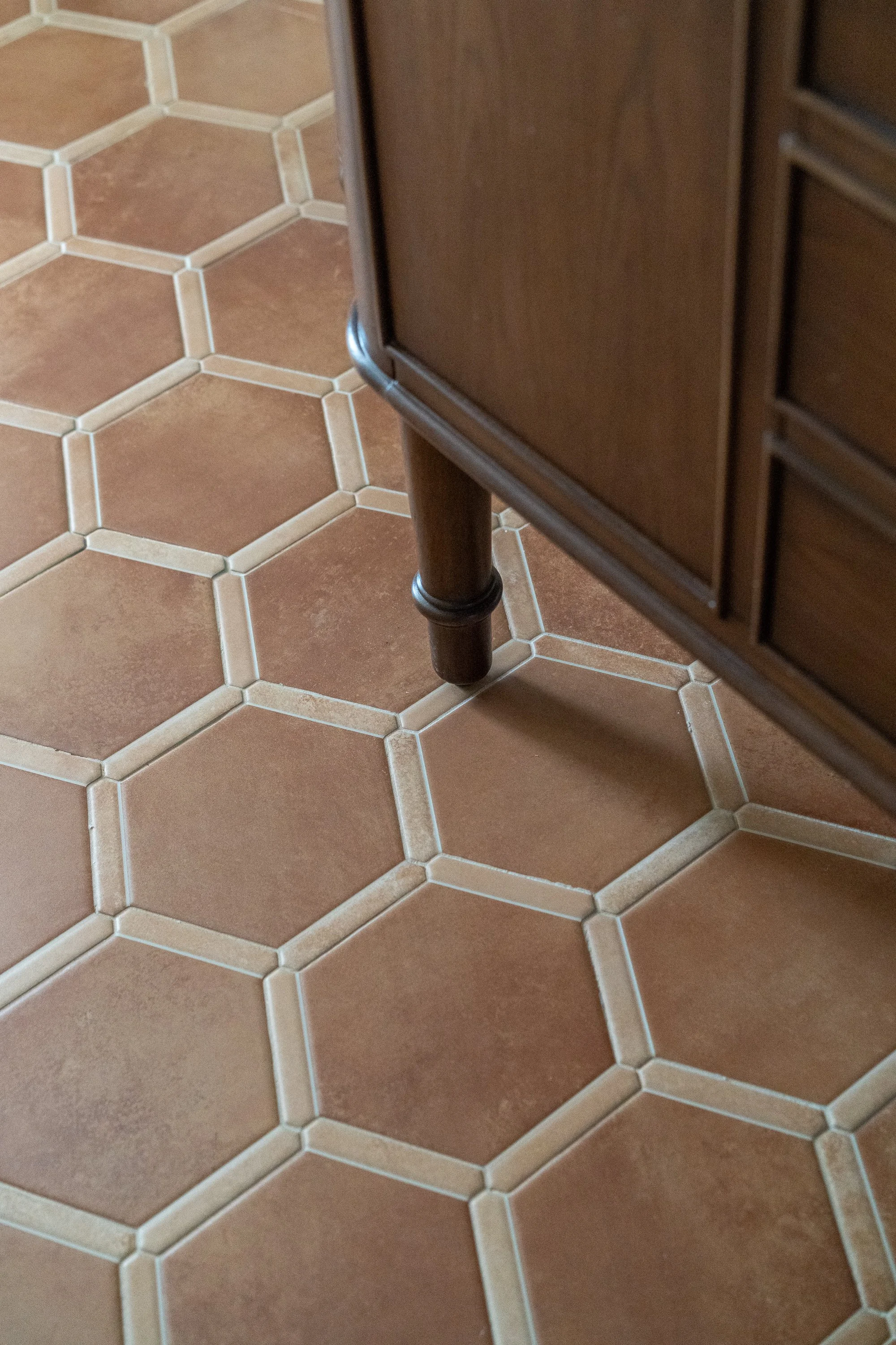 Close-up of a brown hexagonal tiled floor next to a piece of wooden furniture with a turned leg.