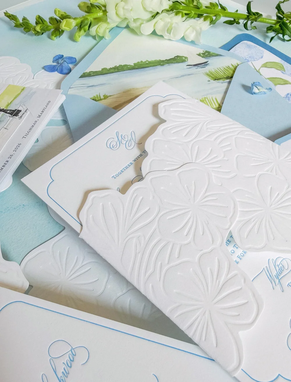 White sculpted floral invitation wrap with delicate blue printed details and a watercolor coastal envelope liner