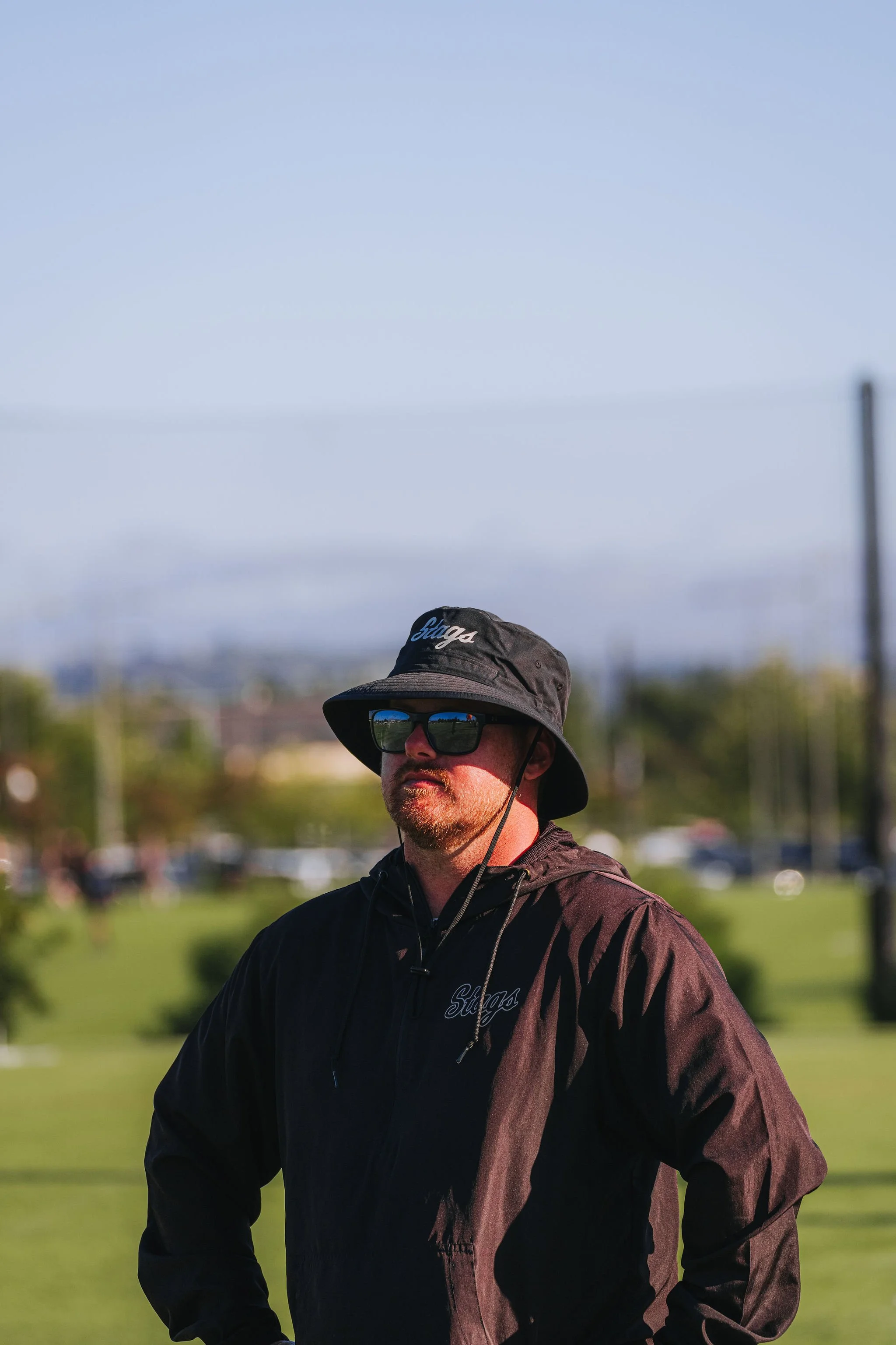 A man wearing a black jacket, sunglasses, and a wide-brimmed hat with 