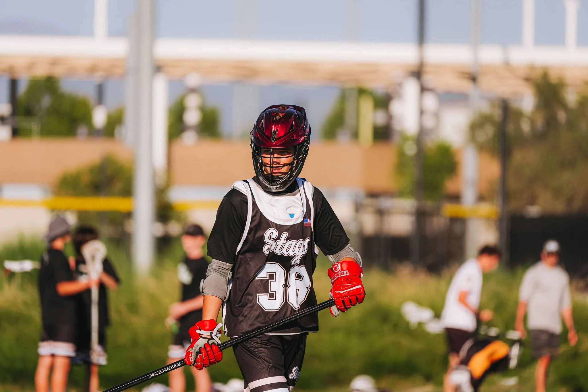 A young hockey player wearing a helmet, gloves, and a jersey with the number 36, holding a hockey stick, and smiling during a game or practice outdoors.