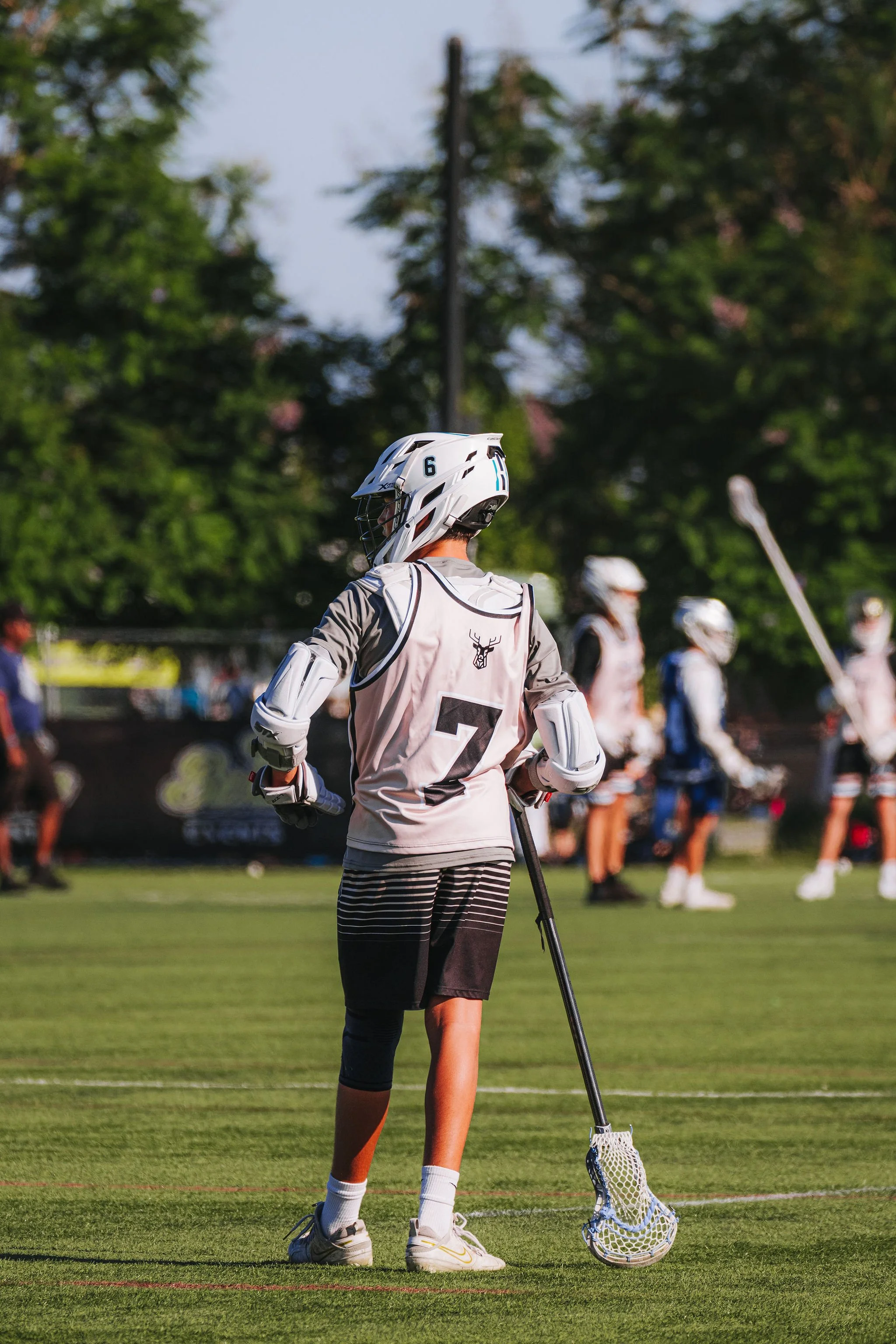A lacrosse player wearing a helmet and sports gear holding a lacrosse stick on a grass field during a game.