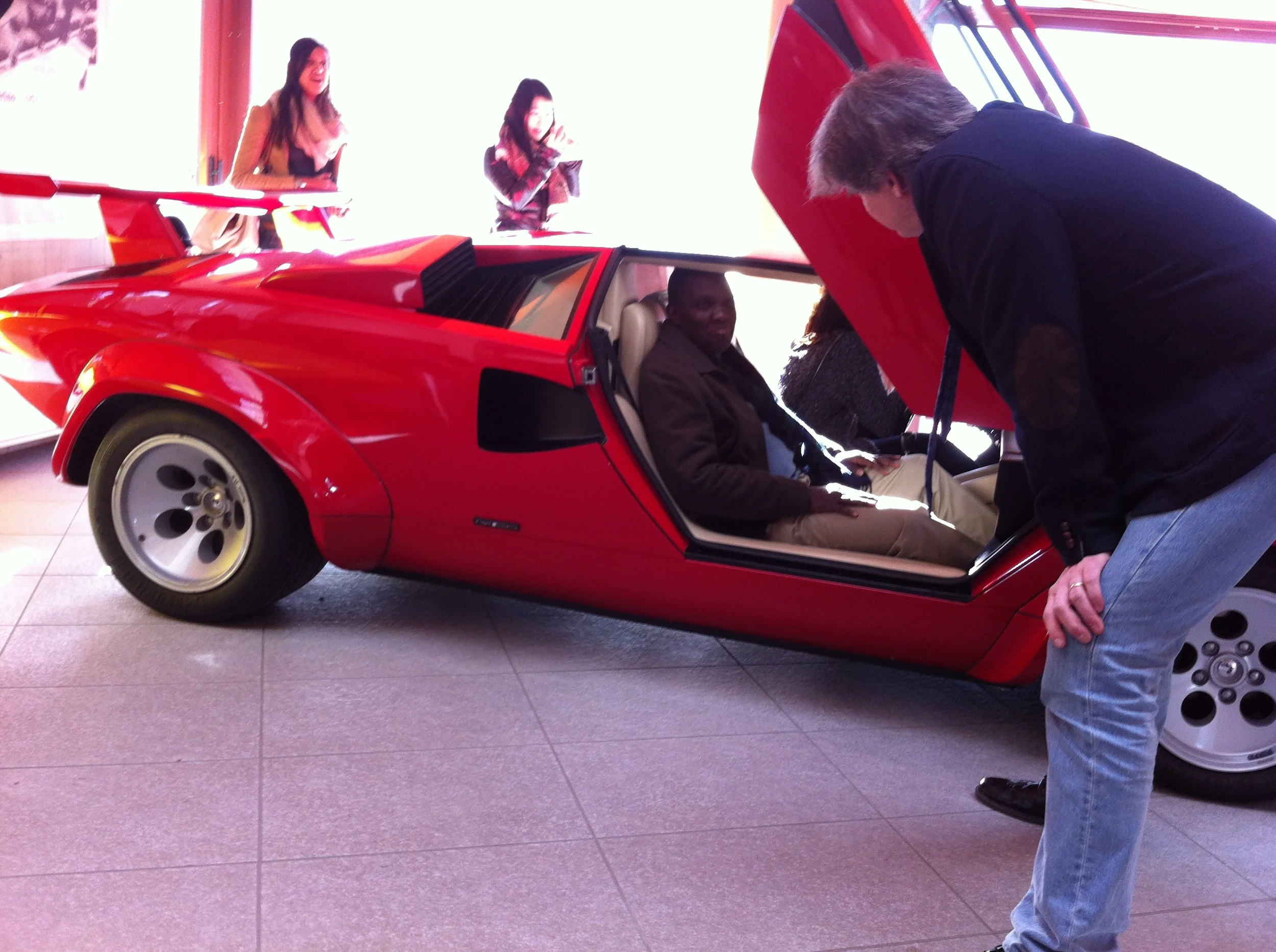 Students examining a red sports car with a designer during an automotive design studio visit