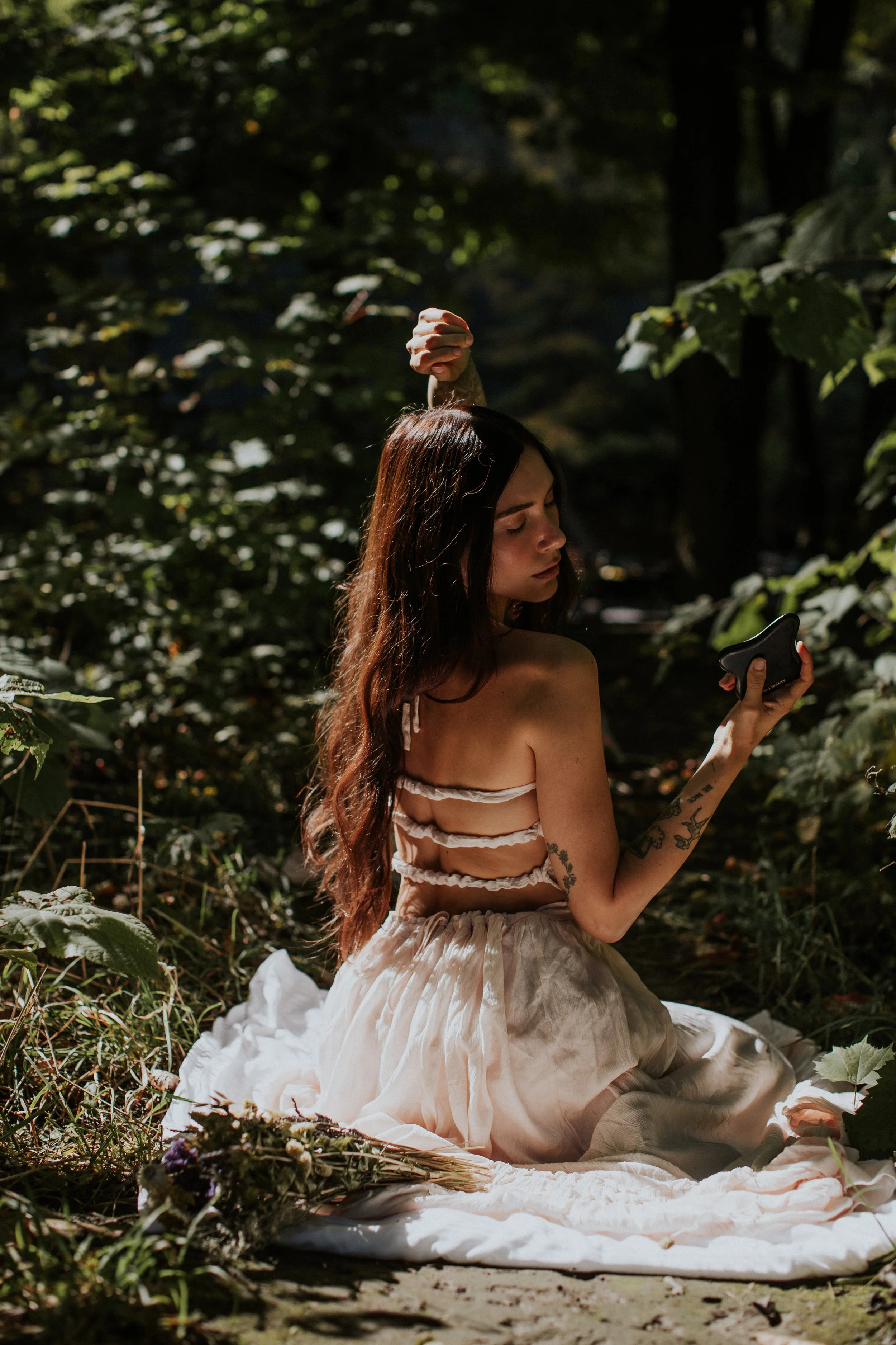 facesbykatey sitting in forest with gua sha stone