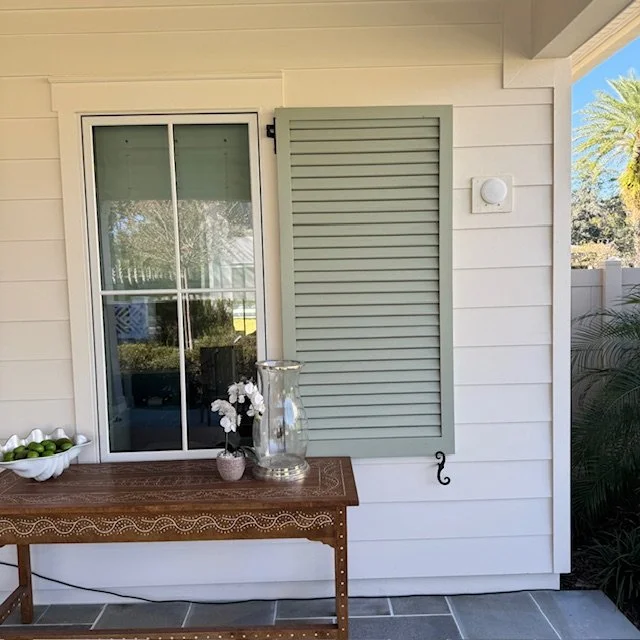 Handcrafted light green louvered wood shutter mounted beside a window on a Palm Valley Ponte Vedra Beach home, adding coastal character and function.
