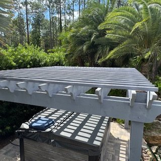 Custom painted wood pergola installed over a backyard spa, surrounded by tropical landscaping and palm trees.