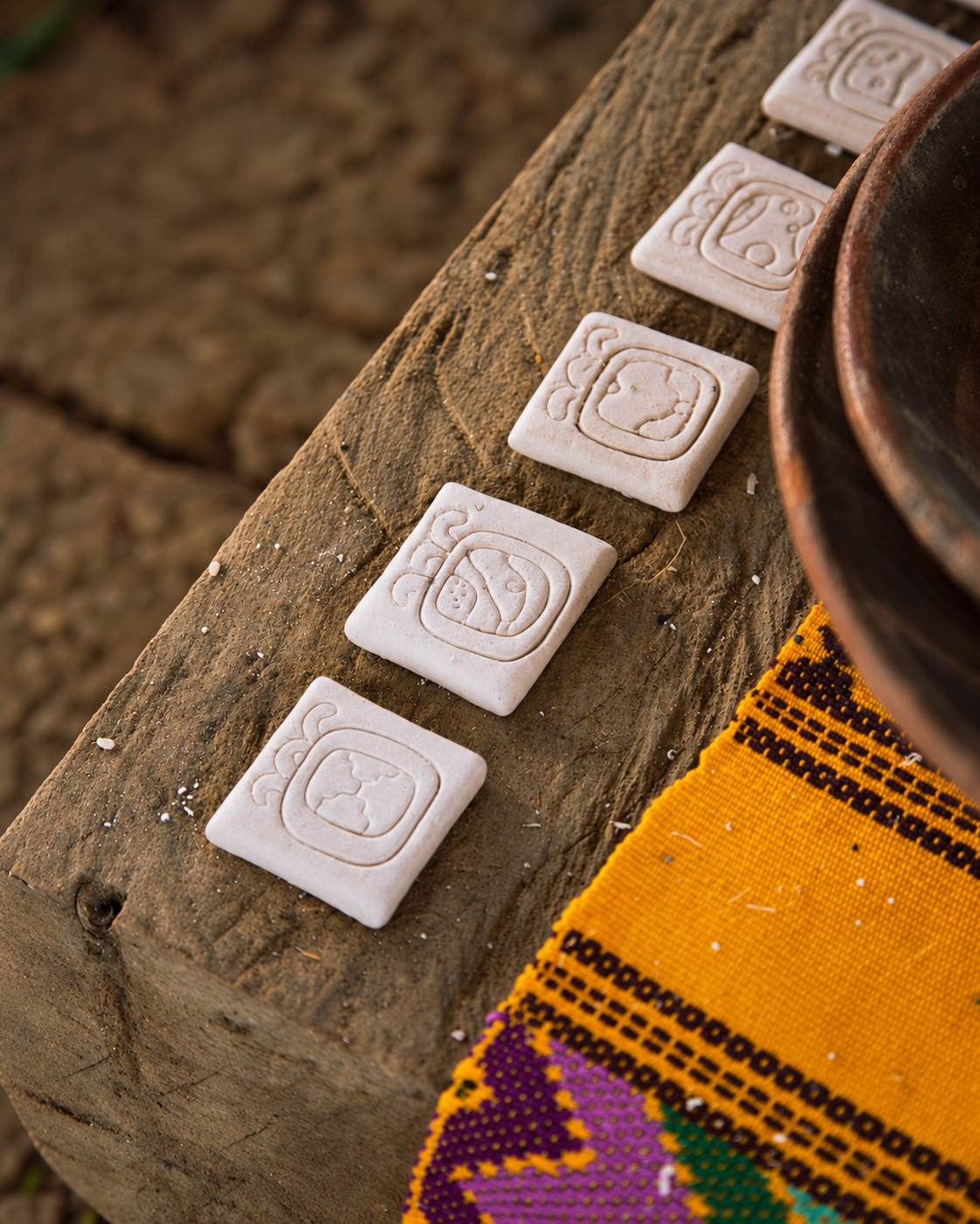 Handmade glyph pieces of the Maya Cholq’ij arranged on wood beside a woven textile.