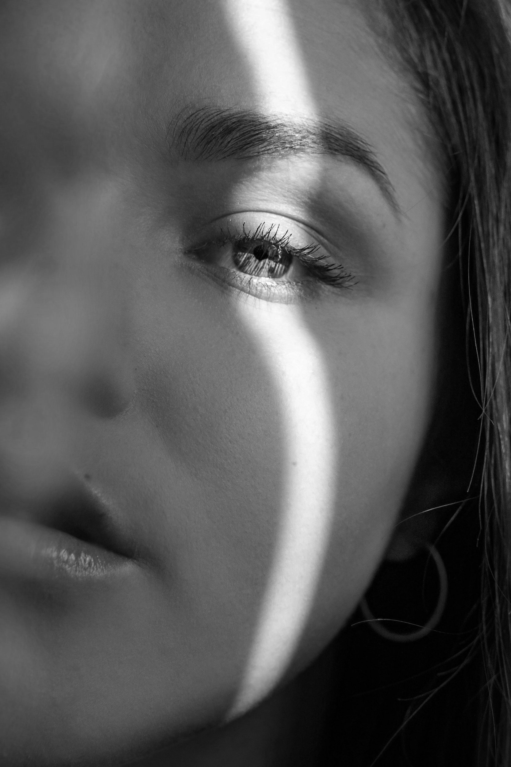 Close-up of a woman's face in black and white with a shadow cast across her eye, highlighting her eye, eyebrows, and lips.