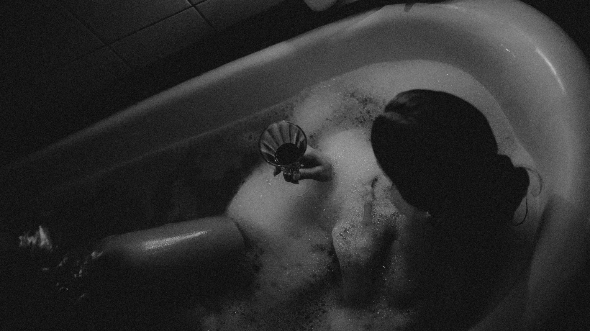A woman relaxing in a bathtub filled with bubbles holding a glass in her hand.