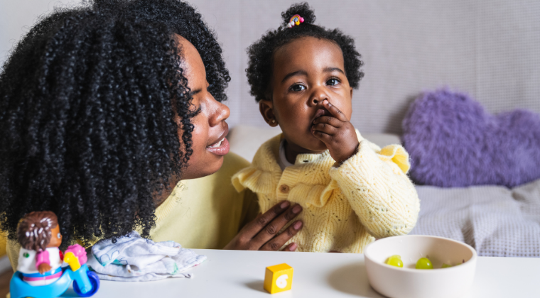 Mother watching baby putting a piece of fruit in her mouth