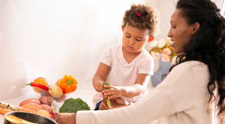 Mother preparing food with her daughter sitting next to her on the kitchen counter