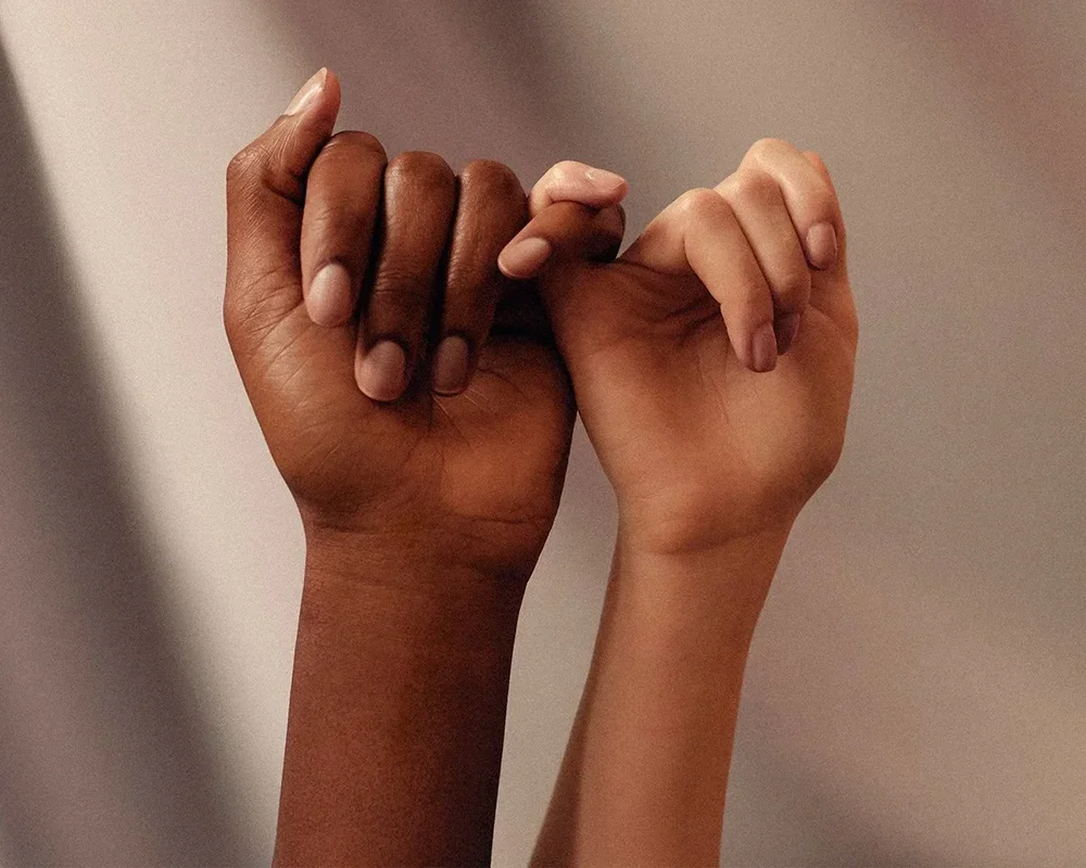 Hände zweier Personen, kleine Finger verschränkt, symbolisieren Partnerschaft und Verbindung